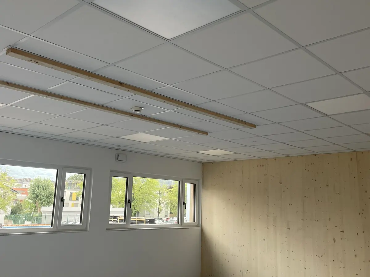 Raum im Betriebskindergarten der Salzburg AG mit Rasterdecke, Vorsatzschalen und Holzwandverkleidung